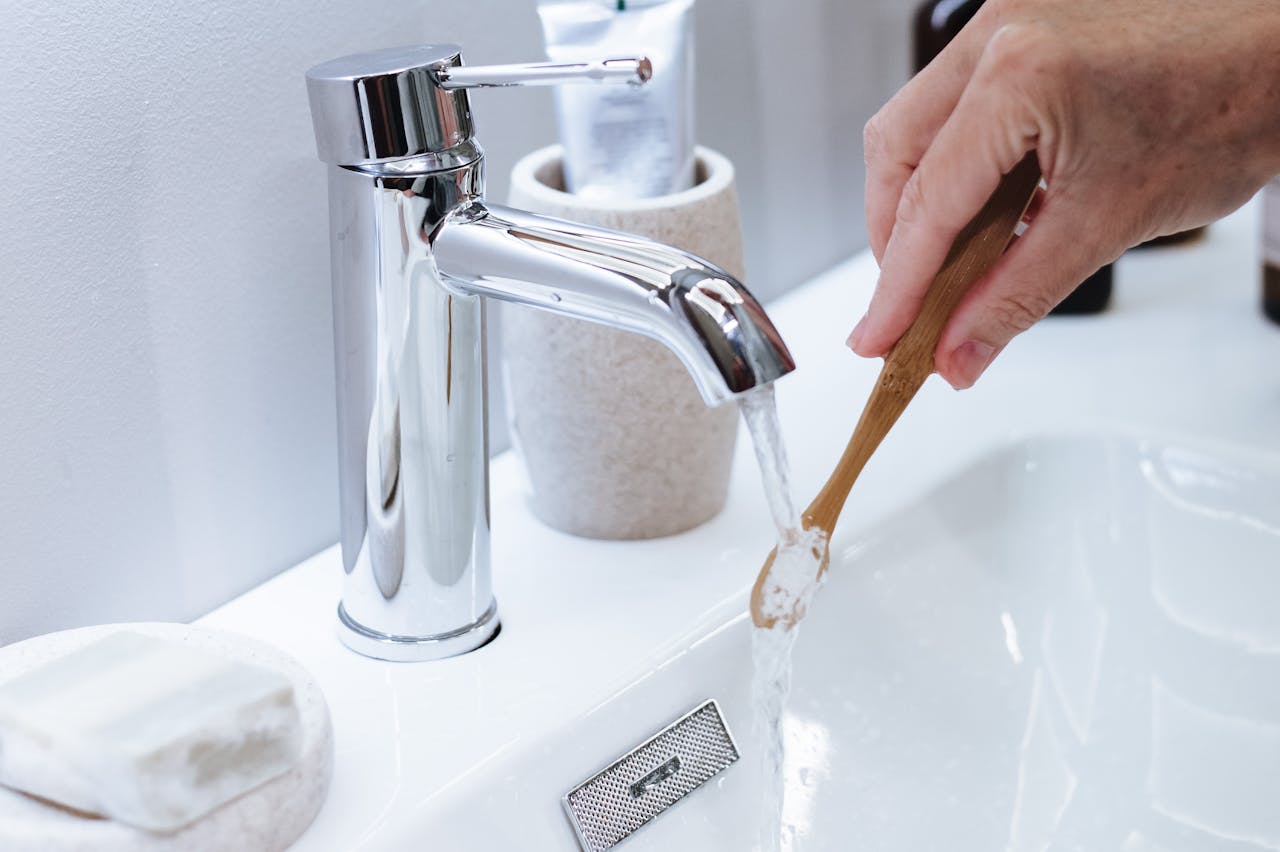 A hand rinsing a bamboo toothbrush under a modern bathroom faucet. Eco-friendly dental care.